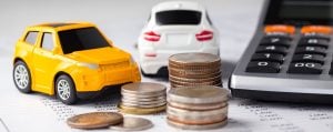 Toy cars, stacked coins, and a calculator on financial documents symbolize car finance planning.