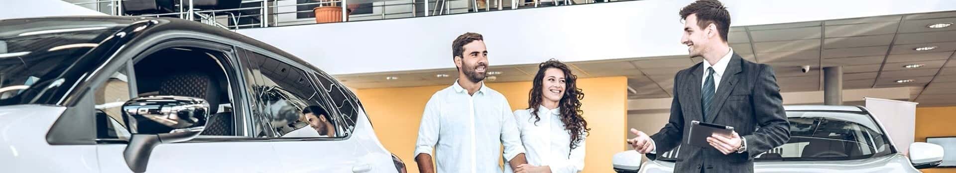 Salesperson talking with a smiling couple in a car showroom.