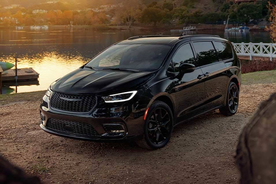 Black minivan parked by a serene lake at sunset, reflecting vibrant autumn scenery.