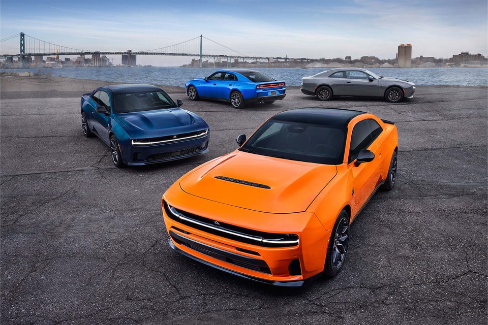 Four modern sports cars in various colors parked by a waterfront with a bridge in the background.