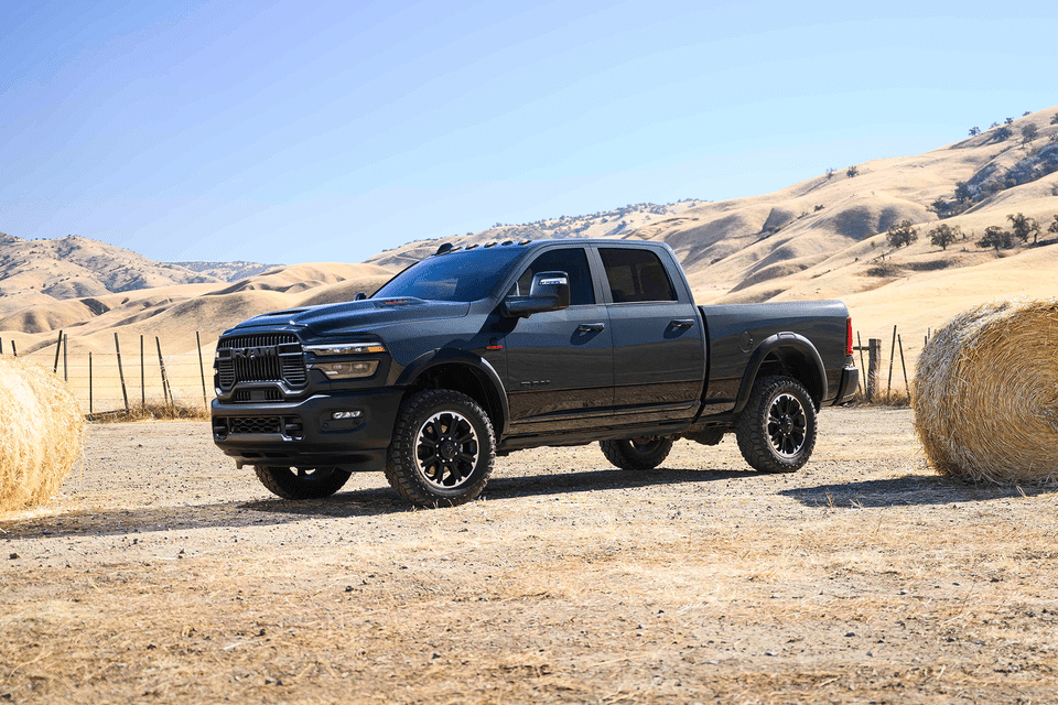Black pickup truck parked in a rural landscape, with hay bales and rolling hills in the background.
